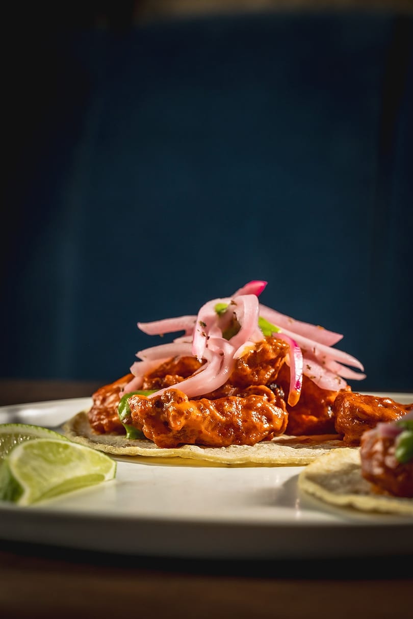 Close-up of a vibrant chicken taco topped with pickled red onions and lime wedges.