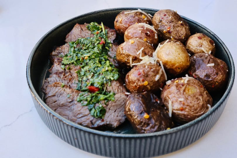 Steak with green chimichurri sauce and roasted baby potatoes topped with cheese and chili flakes.