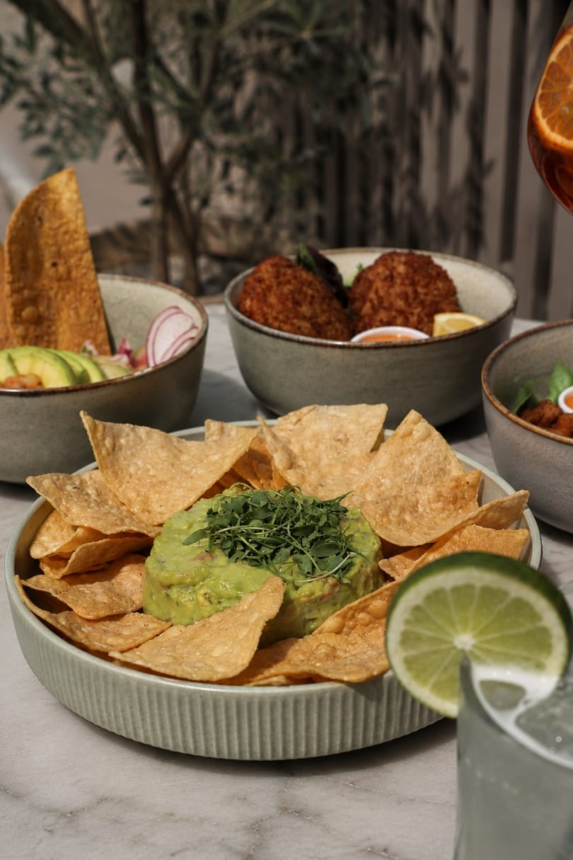 Guacamole with tortilla chips, ceviche, and fried croquettes on a marble table.