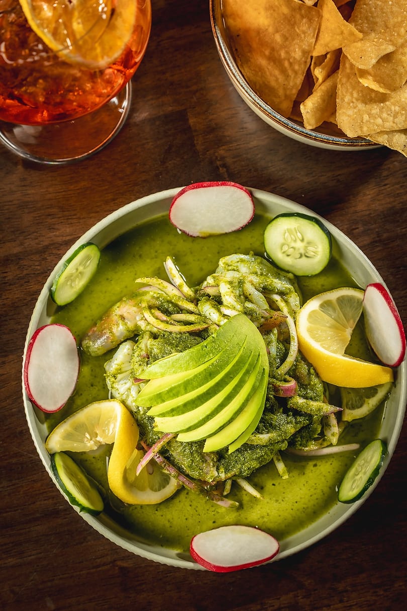 Green ceviche with shrimp, avocado, radishes, cucumbers, and lemons, served with tortilla chips.