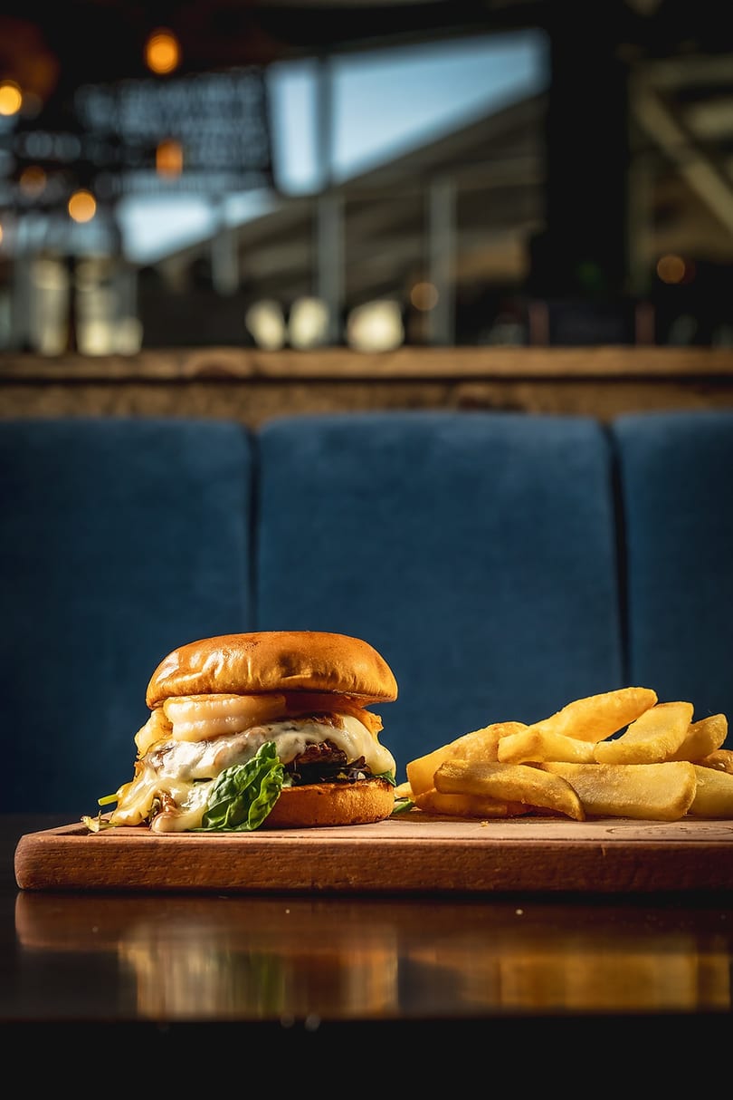 Gourmet burger with melted cheese and fries on a wooden board in a restaurant setting.