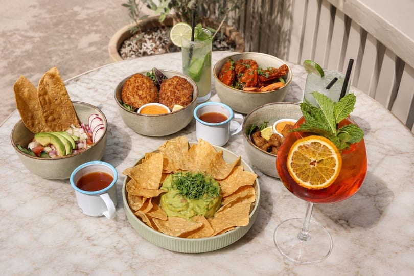 A marble table laden with various bowls of food, including guacamole, ceviche, and fried items, plus cocktails.