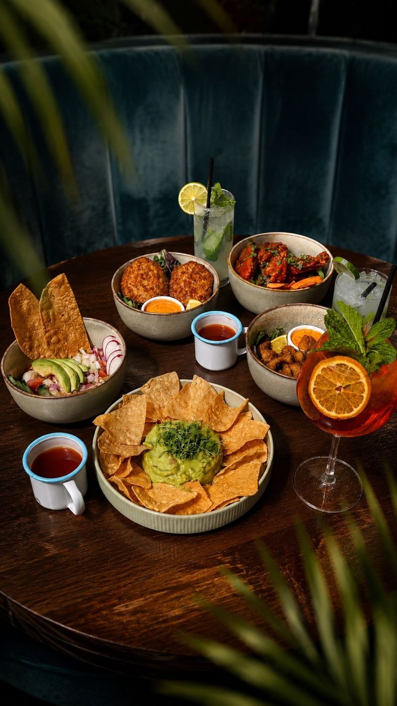 A wooden table laden with various dishes, including guacamole, ceviche, and cocktails.